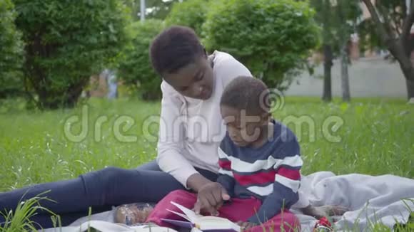 肖像迷人的非裔美国妇女坐在毯子上她的小儿子在公园里年轻的母亲视频的预览图