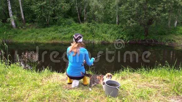 金发女人和可爱的猫宠物在池塘岸边钓鱼视频的预览图