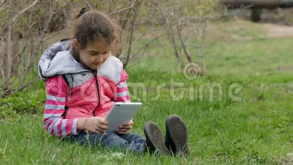 坐在草地上玩平板电脑的少女视频的预览图