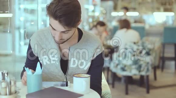 坐在咖啡馆里拿着平板电脑的年轻人视频的预览图