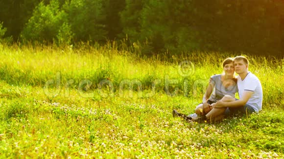 年轻幸福的夫妇坐在公园的绿草地上梦想着拥有自己的房子抵押概念视频的预览图