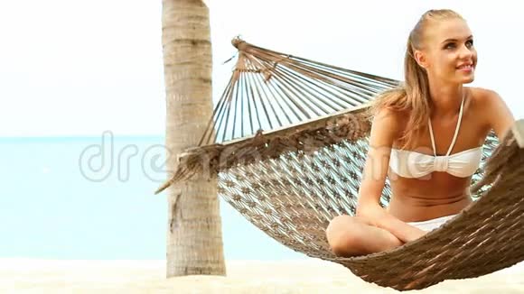 美丽的微笑的女人一头金发坐在吊床上交叉腿视频的预览图