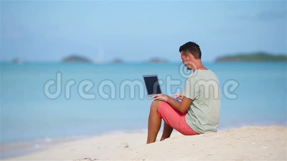 带笔记本电脑的年轻人在加勒比海热带海滩坐在沙滩上用电脑工作的人视频的预览图