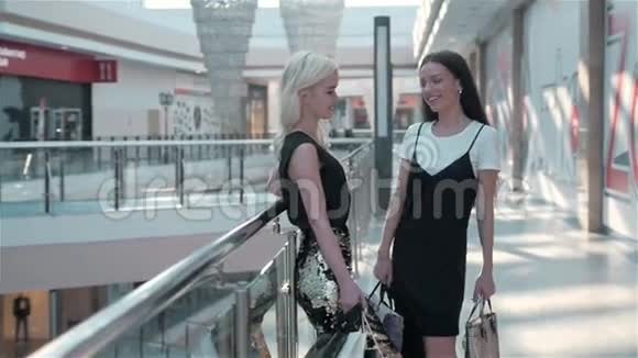 两个正在购物的女朋友站在自动扶梯上手里拿着袋子时尚女购物视频的预览图
