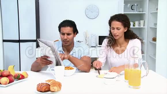 男人一边看报纸一边和女友吃早餐视频的预览图