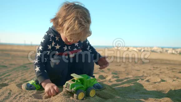 这个男孩正在海滩上玩一辆绿色的玩具自卸卡车视频的预览图