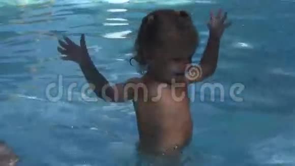 美丽的宝宝很快乐笑着用蓝色的水拍着她站在水池边的手视频的预览图