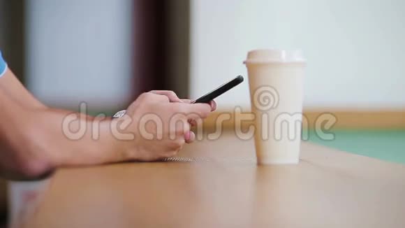 在咖啡馆里男人手拿着手机和一杯咖啡的特写镜头使用移动智能手机的人一个男孩摸着屏幕视频的预览图