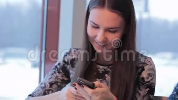 智能手机女孩在手机上使用应用程序在咖啡馆里微笑地喝咖啡视频的预览图