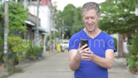 快乐的成熟男人在户外的街道上用电话微笑视频的预览图