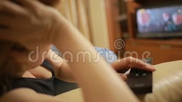 美丽的女人坐在家里的沙发上看电视改变频道视频的预览图