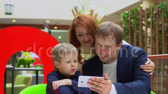 技术和人的概念幸福的年轻家庭与购物袋和智能手机爸爸和儿子一起购物视频的预览图