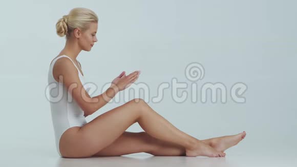 年轻美丽健康和自然的金发女人穿白色泳衣涂上护肤霜按摩护肤脂肪视频的预览图