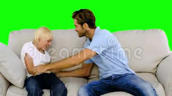 父亲在绿屏上的沙发上挠着儿子视频的预览图