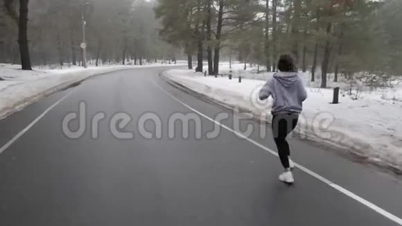 年轻迷人的白种人女孩在冬天带着耳机在雪地公园跑步后面跟着视频的预览图