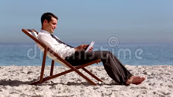 用平板电脑微笑商人在海滩上放松视频的预览图