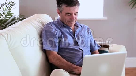 成熟的男人坐在沙发上用笔记本电脑接电话视频的预览图