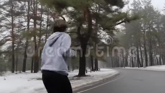 年轻迷人的白种人女孩在冬天带着耳机在雪地公园跑步后面跟着视频的预览图