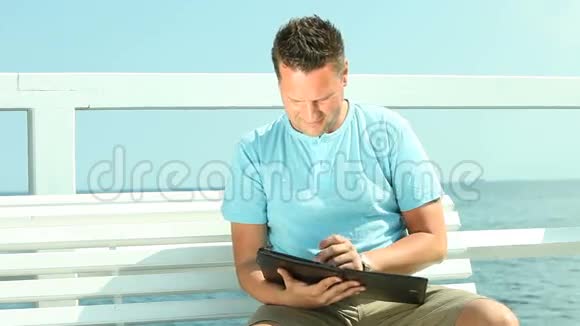 坐在长凳上的人在海上用平板电脑视频的预览图