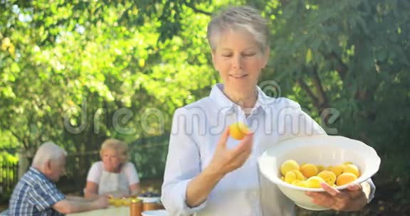 在花园里拿着一碗杏子的老妇人视频的预览图