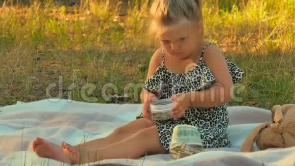 可爱的小女孩在夏天公园的毯子上玩钱视频的预览图