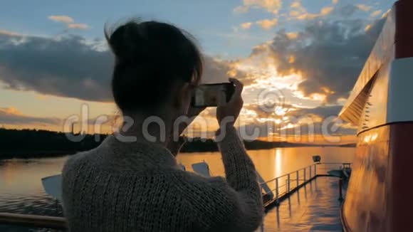 女轮廓用智能手机在游轮甲板上拍摄日落照片视频的预览图