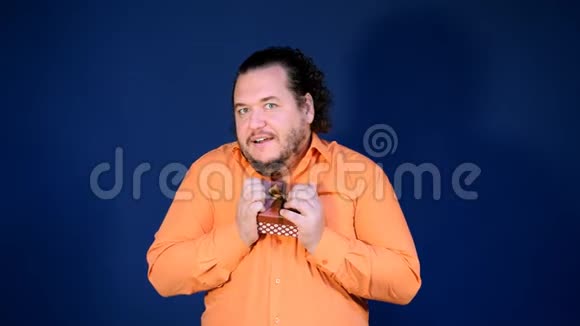 穿着橙色衬衫的滑稽胖子打开一个带礼物的盒子视频的预览图