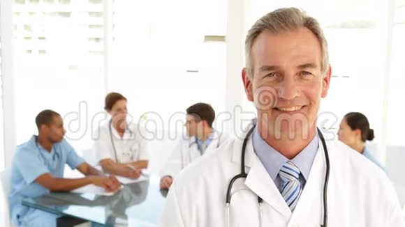 快乐的医生看着摄像机和他身后的工作人员视频的预览图