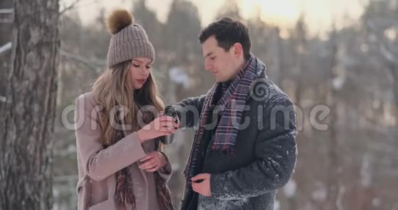 快乐的一对夫妇捧着热茶杯在冬天的风景年轻的情侣在寒假里站在一个视频的预览图