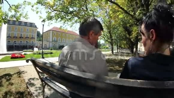 一对夫妇坐在公园的长椅上度过一个愉快的夏日视频的预览图
