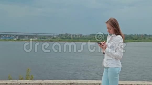 美丽的女孩站在河堤上打着电话视频的预览图