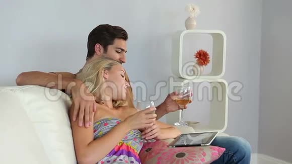 微笑的情侣躺在沙发上用平板电脑喝酒视频的预览图