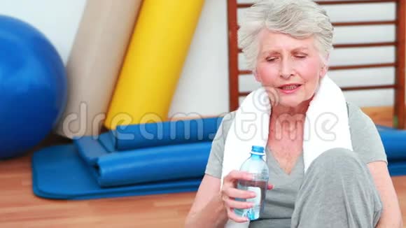 坐在地板上喝水的老年妇女视频的预览图