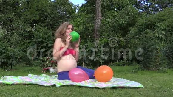 漂亮的孕妇女孩在花园里吹五颜六色的气球视频的预览图