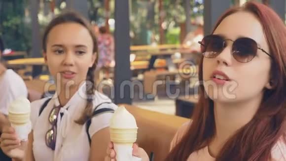两个年轻的女人吃冰淇淋坐在户外咖啡馆里她们玩得很开心4K慢动作稳定视频的预览图