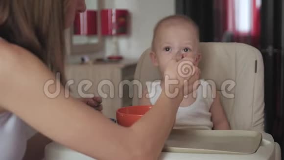 妈妈用勺子喂她的小儿子妈妈在家里给她可爱的孩子提供健康的食物快乐的小男孩视频的预览图