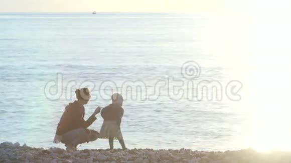 母亲和孩子把鹅卵石扔进海里视频的预览图
