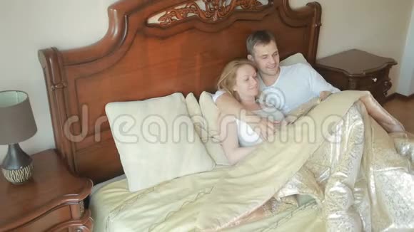 两个男人和女人躺在卧室的床上一起大声读这本书视频的预览图