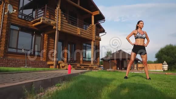 一位身材苗条穿着运动服的漂亮女士正准备在她附近的草坪上开始训练视频的预览图