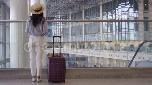 带着行李戴帽子的年轻女子在国际机场随身携带行李机场内的航空乘客视频的预览图