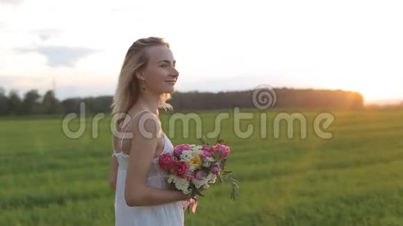 美丽的女人带着一束鲜花走在田野里视频的预览图