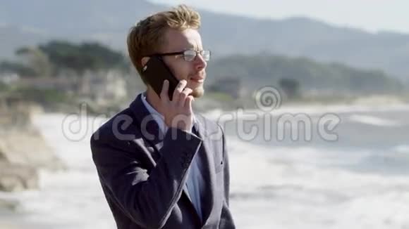 年轻的商人站在太平洋海岸边打电话视频的预览图