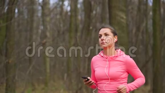 日落时分一群戴着耳机和智能手机的女人在秋天的森林里奔跑慢动作视频的预览图