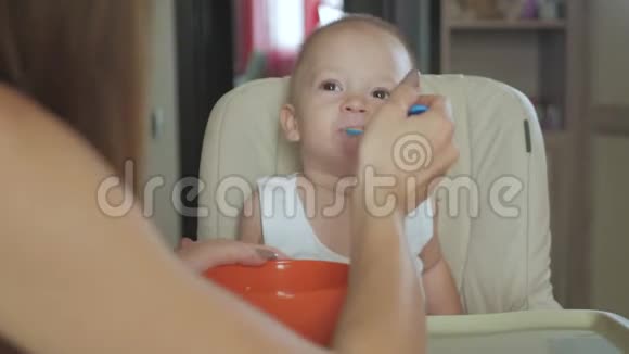 妈妈用勺子喂她的小儿子妈妈在家里给她可爱的孩子提供健康的食物快乐的小男孩视频的预览图