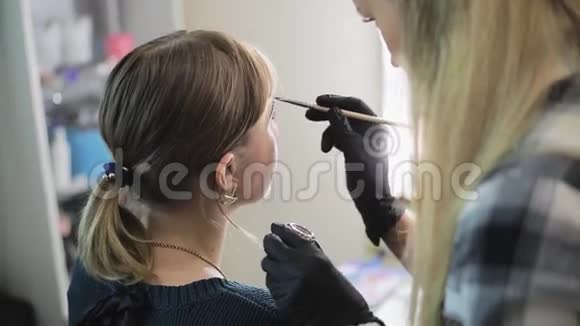 化妆师用专业的画笔在美容院的镜子前给一个漂亮的女孩画眉毛视频的预览图