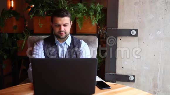 商人在咖啡馆里用手提电脑和电话交谈视频的预览图