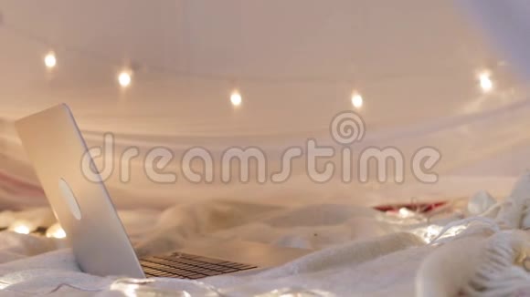 笔记本电脑躺在床上背景是圣诞树灯移动平稳视频的预览图