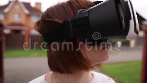 年轻的红头发妇女使用VR头盔智能手机增强现实视频的预览图