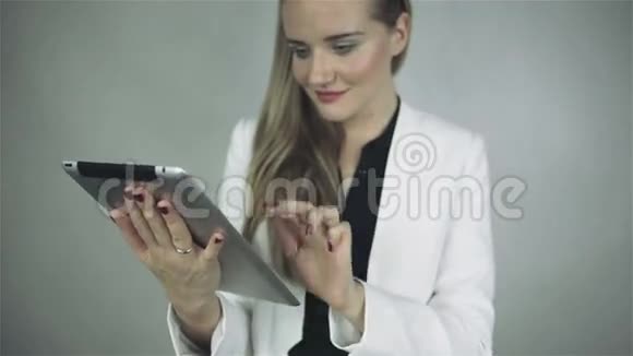 微笑优雅的女人与眼镜站在灰色背景与触摸板视频的预览图