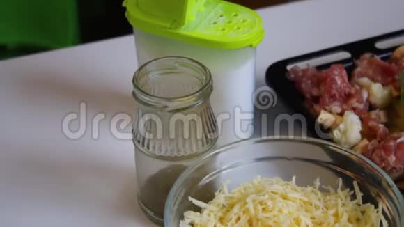 桌子上放着一个烤盘里面装满了土豆菜花和肉末附近有盐磨碎的奶酪和香料视频的预览图
